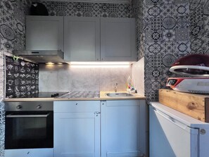 A compact kitchen with a gas stove, a sink, and a microwave. The walls are decorated with patterned wallpaper. - Cosy Cocoon centre de liège (Liege)