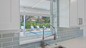 A kitchen with a window overlooking a pool area, featuring a modern faucet and light-colored cabinetry.