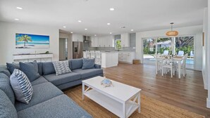 A modern living room with a grey sectional sofa, a white coffee table, and a dining area with white furniture.