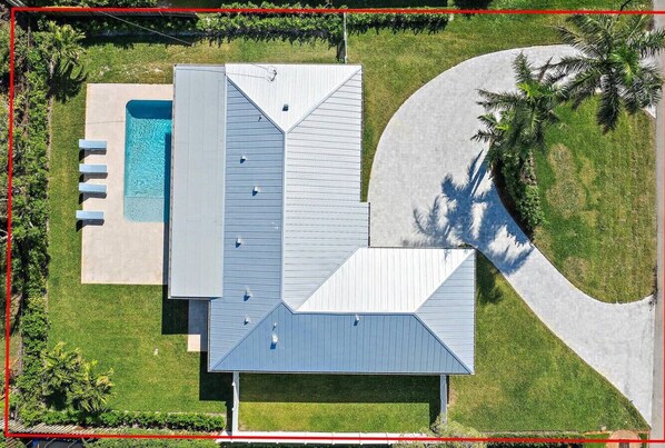An aerial view of a modern building with a swimming pool, a covered patio, and a curved driveway.