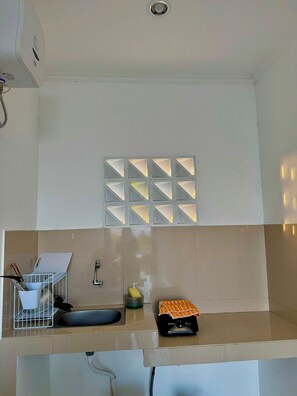 Una cocina con un lavamanos, una pizarra y una ventana pequeña con diseños geométricos.