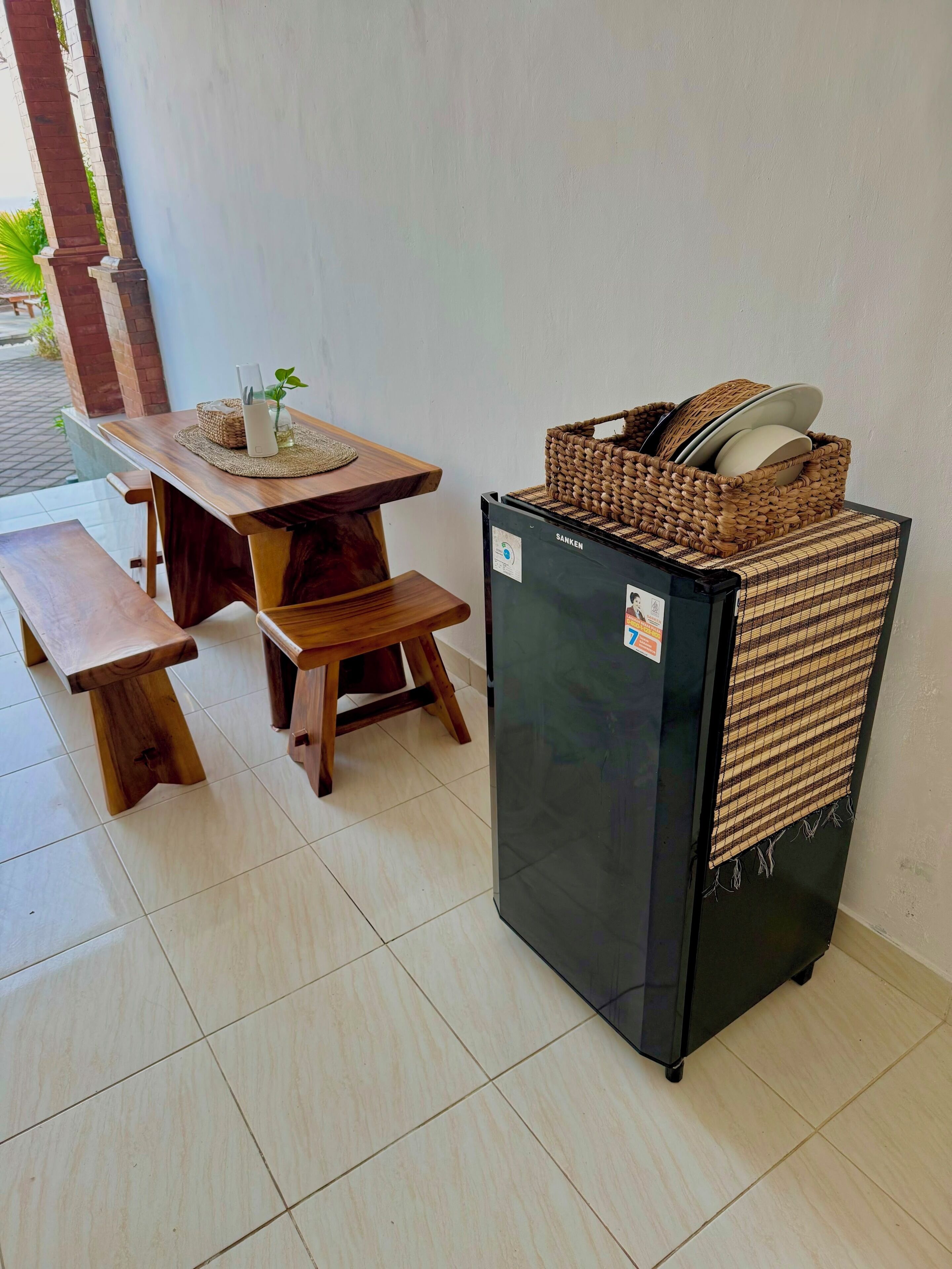 Una mesa de madera con bancos, un refrigerador negro y una cesta tejida encima.