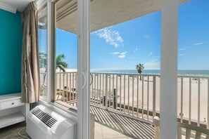 A room with a large window overlooking a beach, a white air conditioning unit, and a view of the ocean.