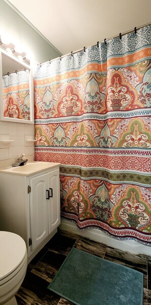 Un baño con una cortina de ducha estampada, un lavamanos blanco y un tapete verde.