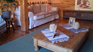 A cozy living room with a wooden ceiling, a cushioned sofa, a coffee table with decorative items, and a potted plant. - Large gîte for 14 people with hot tub & fireplace 🌲 Nature, forest & relaxation (raon sur plaine)