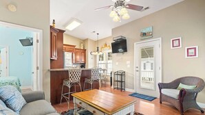 A living room with a sofa, a wooden coffee table, and a dining area with chairs and a TV. - Branch Breeze - Golf Cart | Linens | Ocean Lakes (Myrtle Beach)