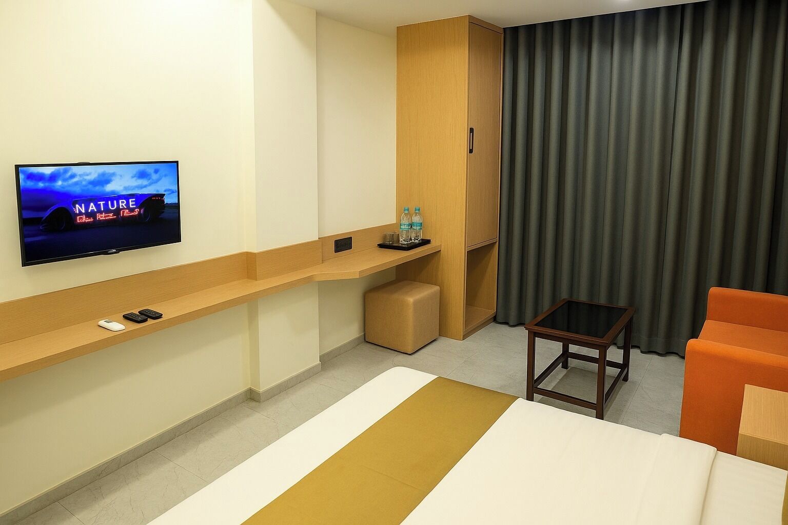 Une chambre d’hôtel avec un lit, un téléviseur fixé au mur, une petite table, une chaise et une armoire.