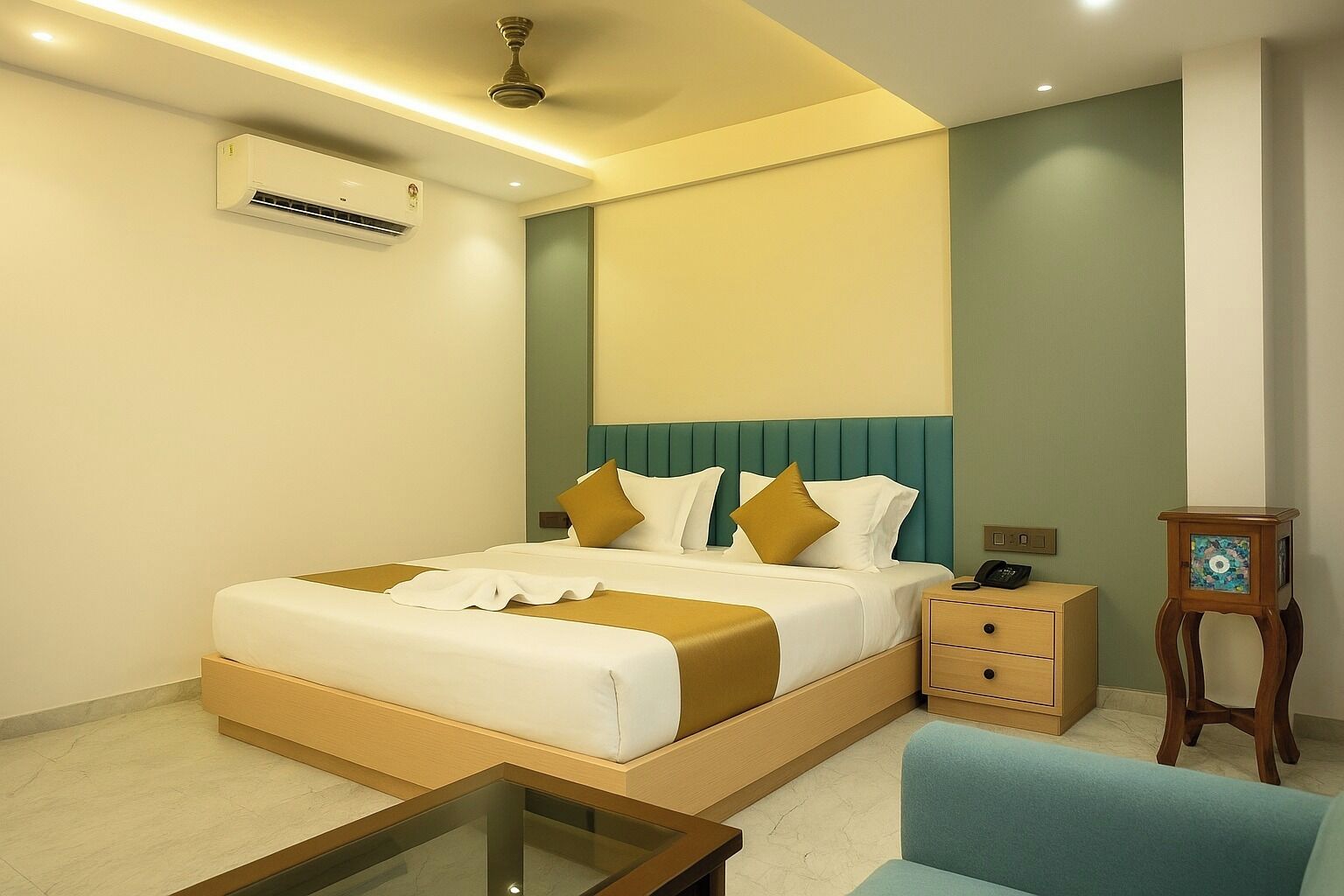A hotel room with a bed, bedside tables, a chair, an air conditioning unit, and a small table.