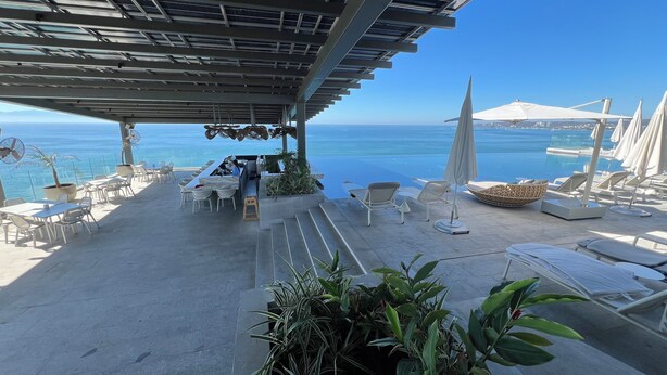 A seaside terrace with outdoor seating, a bar, and a pool.
