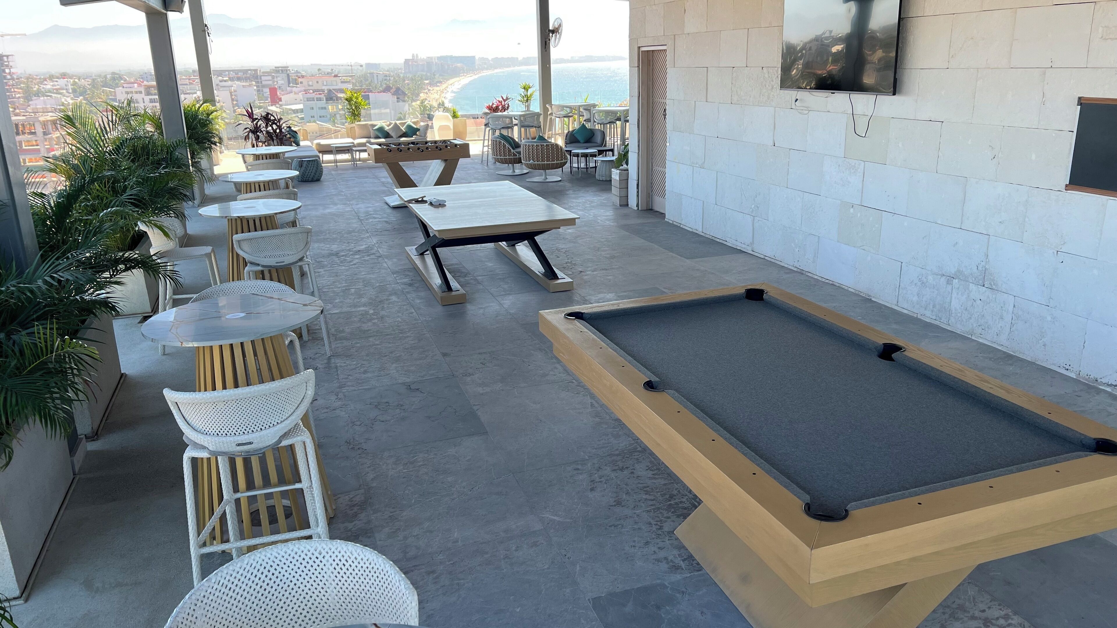 Un salon sur le toit avec des tables de billard, des sièges et une vue sur l’océan.