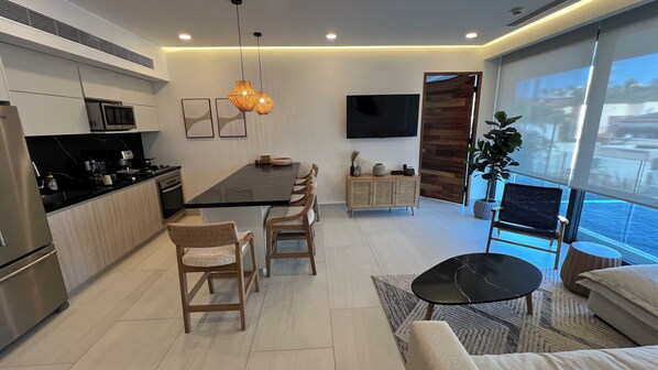 A modern kitchen with a dining area, a flat-screen TV, and a large window with a view.