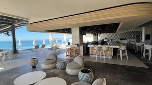 A beachside restaurant with outdoor seating, a bar, and a view of the ocean.