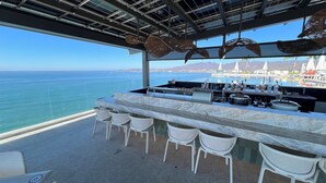 A bar with a view of the ocean, white wicker chairs, and a marble countertop.