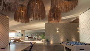 A modern indoor space with a foosball table, a ping pong table, and a bar area.