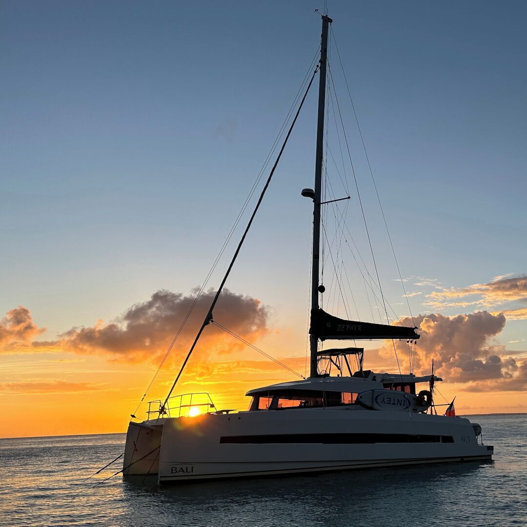 Uno yacht bianco con la scritta "ZERIY" e "BALI" sul fianco, che naviga su acque calme al tramonto.