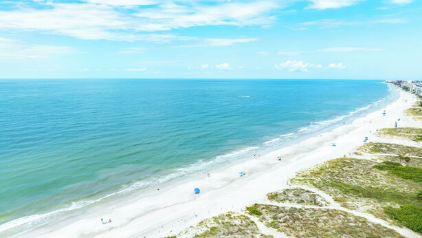 A beach with a long stretch of white sand, clear blue water, and a few umbrellas.
