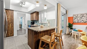 A modern kitchen with a central island, wooden cabinets, and a dining area with colorful chairs.
