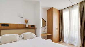 Ein modernes Hotelzimmer mit einem großen Bett, einem Holz-Kopfteil, einem Nachttisch mit einer Vase, einem Spiegel und einem Kleiderschrank.