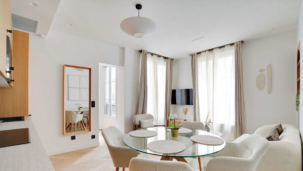 Ein modernes Wohnzimmer mit einem Glastisch, umgeben von Stühlen, einer Couch und einem an der Wand befestigten Flachbildfernseher.