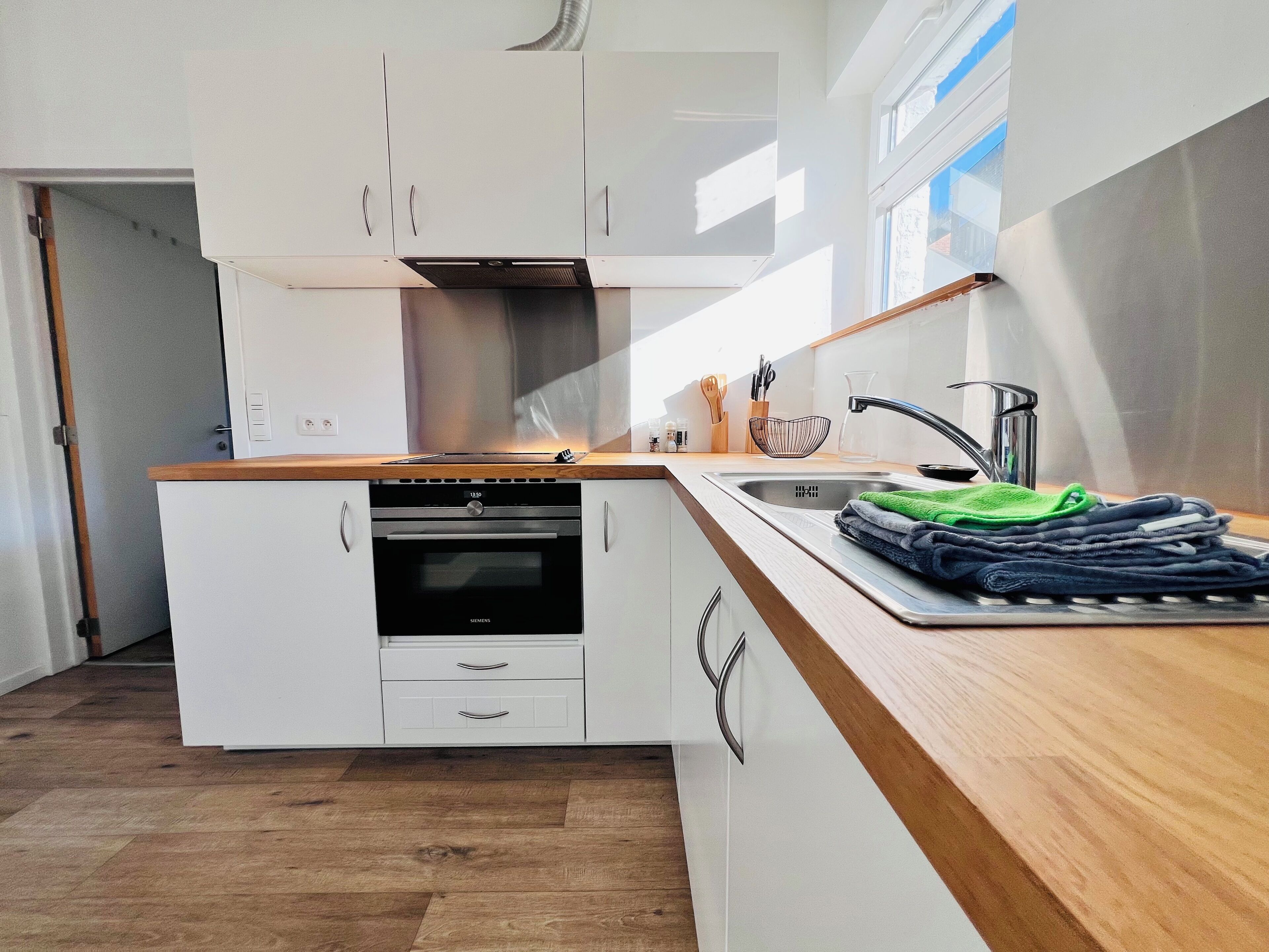 A modern kitchen with white cabinetry, a stainless steel range hood, a built-in oven, and a wooden countertop.