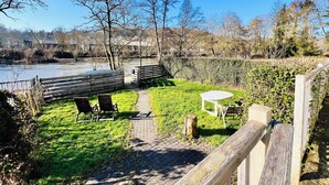 A riverside garden with a wooden deck, chairs, and a table. - Maison proche rivière avec jardin  (Esneux)