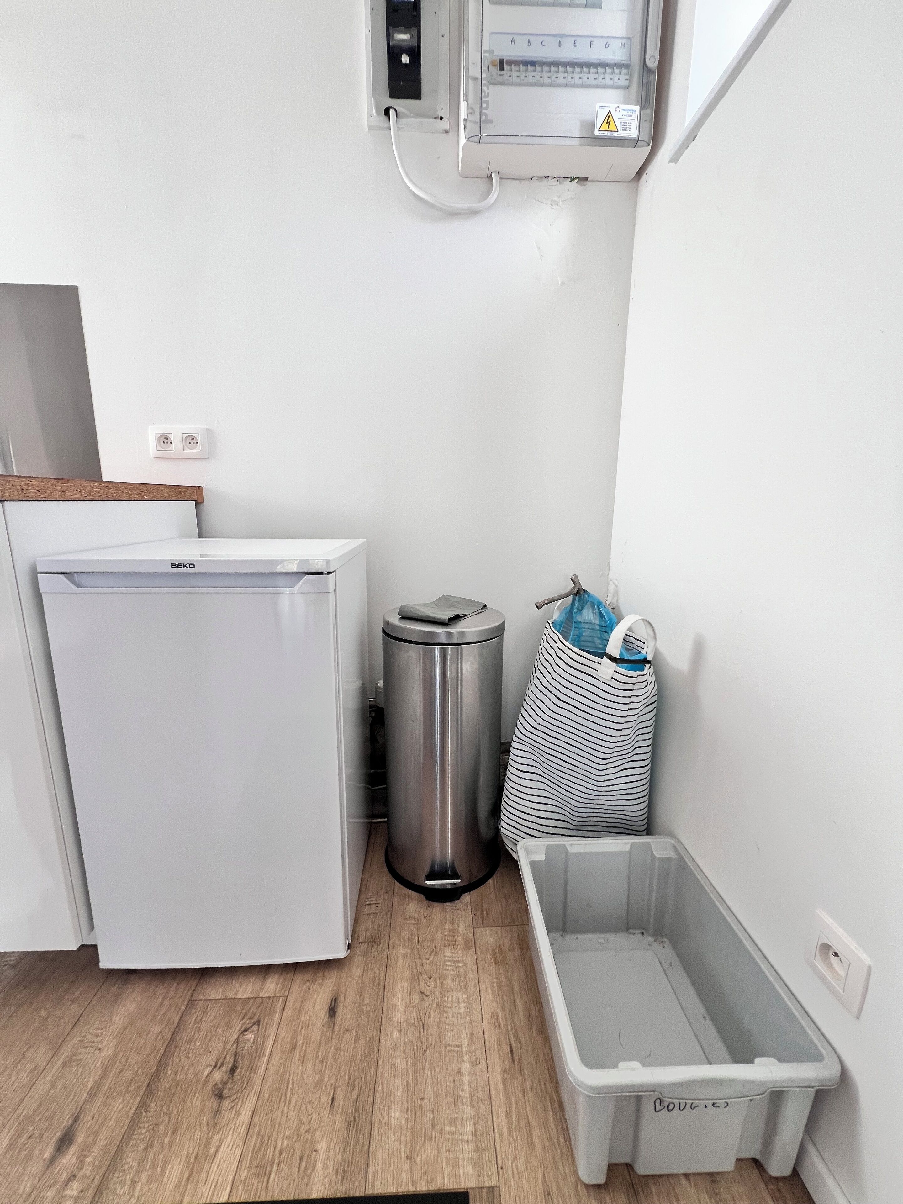 A compact kitchen with a white refrigerator, a stainless steel trash bin, and a gray waste basket.