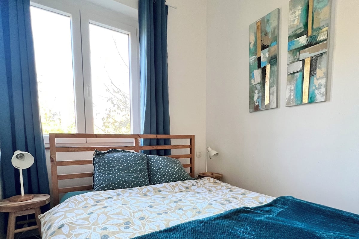 Ein Schlafzimmer mit einem Bett, einem Nachttisch, einer Lampe und zwei abstrakten Bildern an der Wand.
