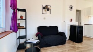 A modern living room with a black sofa, a small round table, a black shelving unit with decorative items, and a kitchen area in the background. - Maison proche rivière avec jardin  (Esneux)