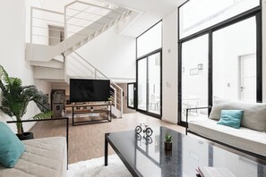 Un salon moderne avec un escalier, un canapé, une table basse et un téléviseur.