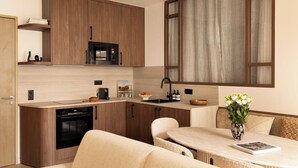 Cocina compacta con armarios de madera, un microondas y un lavamanos. Hay una zona de comedor con una mesa y sillas, y un jarrón con flores sobre la mesa.