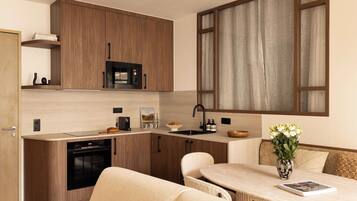 Cocina compacta con armarios de madera, un microondas y un lavamanos. Hay una zona de comedor con una mesa y sillas, y un jarrón con flores sobre la mesa.