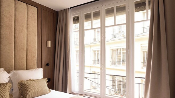 Una habitación de hotel con un ventanal grande, una cama con sábanas blancas y almohadas a rayas.