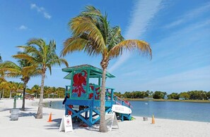 A lifeguard tower with a red octopus mural, situated on a sandy beach with palm trees and a calm body of water in the background.