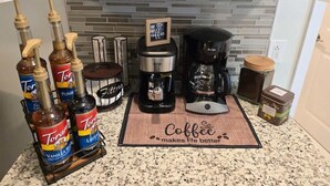 A kitchen counter with coffee-making equipment, including a coffee maker, coffee grinder, and coffee mugs on a shelf. - Bright and Cozy Home in Homestead (Homestead)