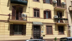 Um edifício com vários andares, varandas, aparelhos de ar condicionado e um carro estacionado.