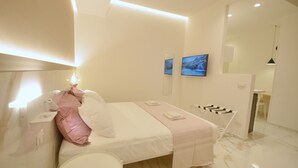 Quarto de hotel moderno com cama, mesa de cabeceira, espelho e um pequeno espaço de estar com uma poltrona e mesa.