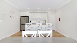 A modern kitchen with white cabinetry, a stainless steel refrigerator, and a dining area with white chairs.