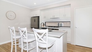 A modern kitchen with white cabinetry, a stainless steel refrigerator, a gas stove, and a white dining table with four chairs.