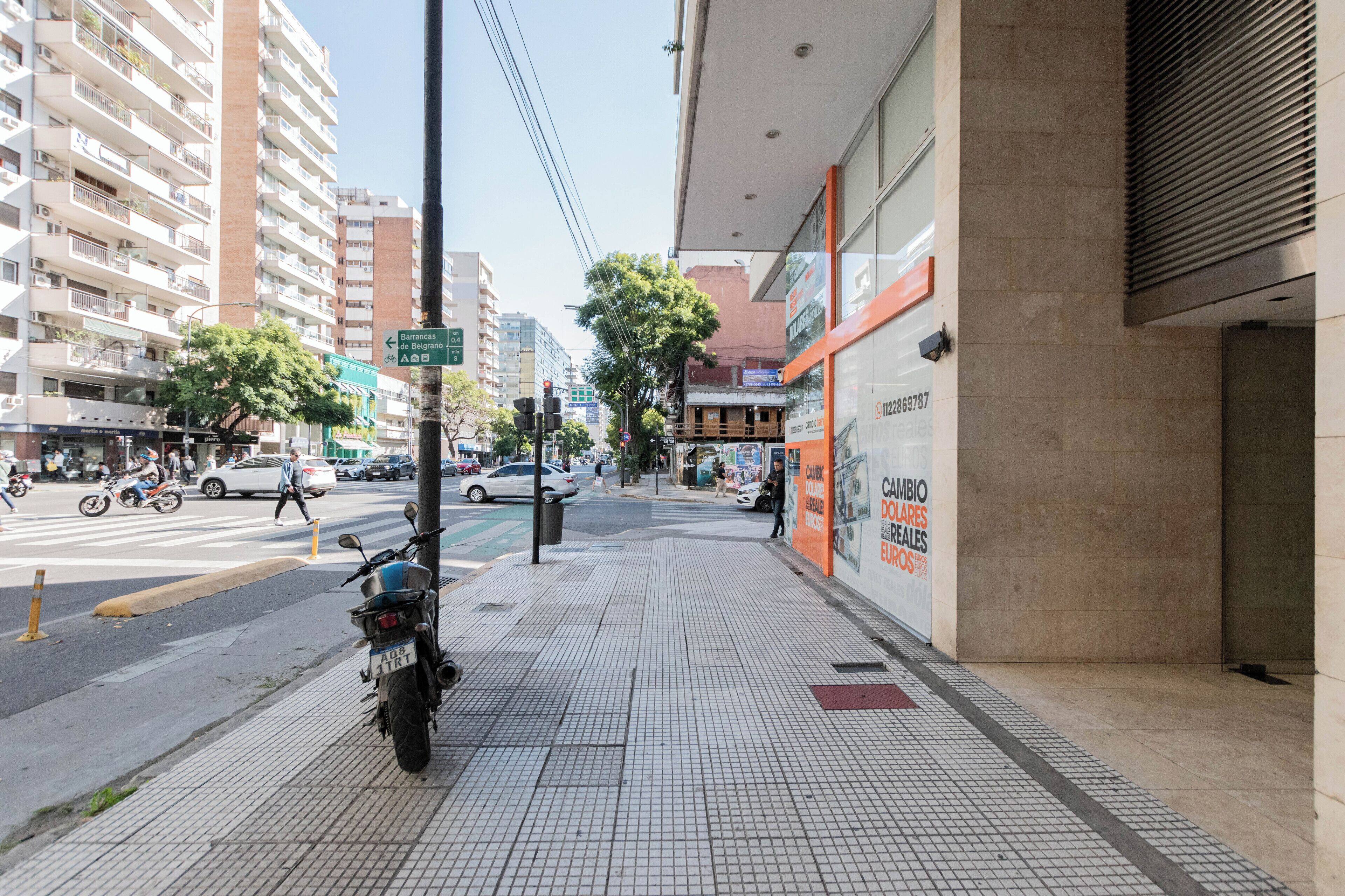 A city street with a motorcycle parked on the sidewalk, buildings, and a pedestrian crossing.