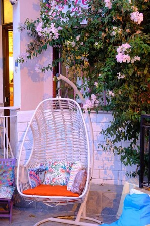 A wicker hanging chair with colorful cushions, a stone wall, and flowering vines. - Yeşim Pansiyon  (Cesme)
