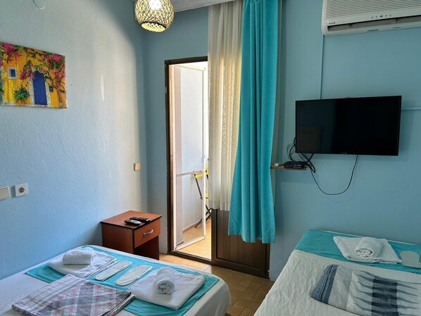 A hotel room with two beds, a TV, a painting, and a sliding door to the outside. - Yeşim Pansiyon (Cesme)