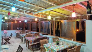 Un restaurant amb diverses taules i cadires, un teulat de palla i llums penjants.