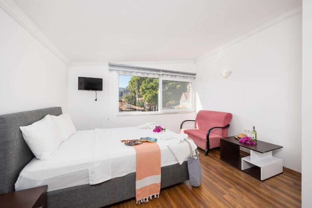A bedroom with a bed, a chair, a small table, a TV, and a window with a view.