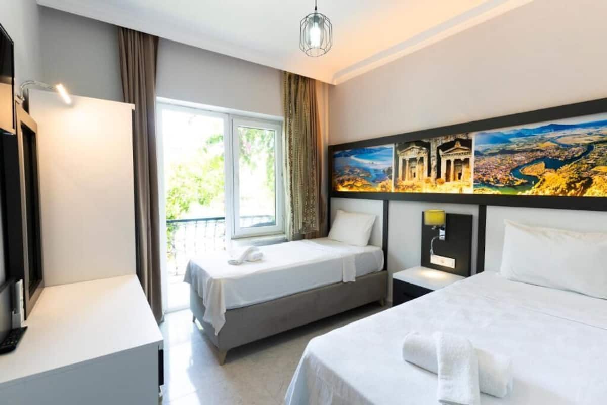 A hotel room with two beds, a TV, a desk, and a large window with curtains.