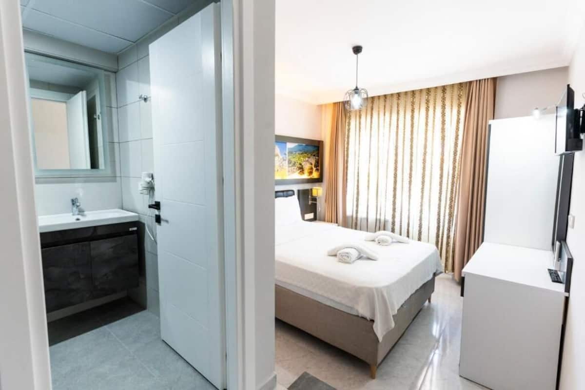 A hotel room with a bathroom, a bed, a TV, and a painting on the wall.
