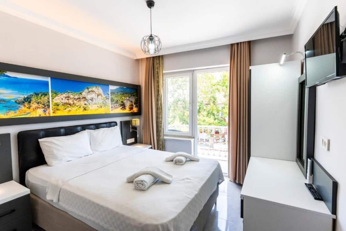 A hotel room with a bed, a desk, a TV, and a painting on the wall.