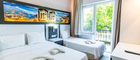 A hotel room with two beds, a desk, a nightstand, and a large window with a view of greenery.