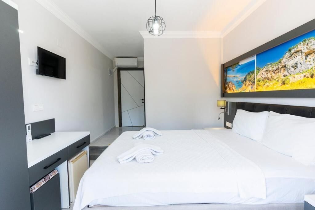 A hotel room with a bed, a desk, a flat-screen TV, and a painting on the wall.
