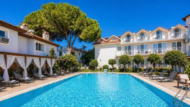 A swimming pool with lounge chairs, a large tree, and a multi-story building with balconies. - Legend Of Dalyan Hotel (Ortaca)