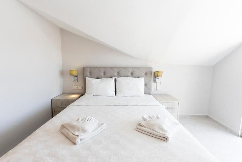 Una habitación de hotel moderna con una cama grande, dos mesitas de noche y un techo inclinado.